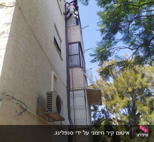 אדם עובד בגובה על בניין עם ציוד בטיחות